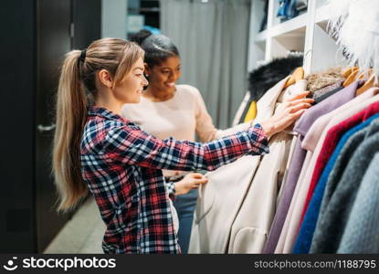 Two girlfriends choosing clothes in shop, shopping. Shopaholics in clothing store, consumerism lifestyle, fashion. Two girlfriends choosing clothes in shop, shopping