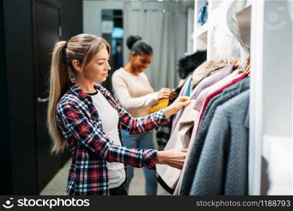 Two girlfriends choosing clothes, shopping. Shopaholics in clothing store, consumerism lifestyle, fashion. Two girlfriends choosing clothes, shopping