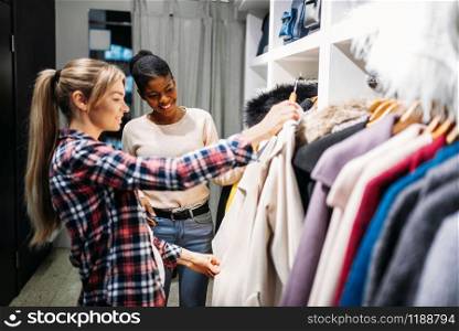 Two girlfriends choosing clothes, shopping. Shopaholics in clothing store, consumerism lifestyle, fashion