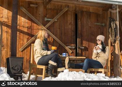 Two girlfriends have tea winter snow cottage sunny outdoor