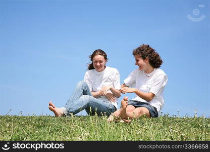 Two girlfriends in white T-shorts have a rest on a grass