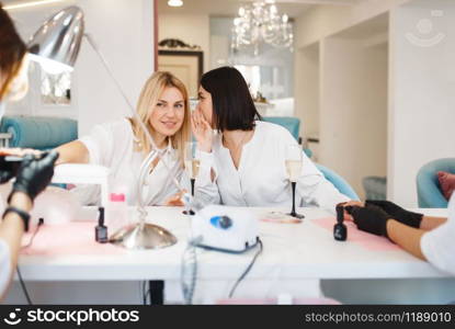 Two girlfriends leisures on manicure procedure in beauty salon. Professional beautician and female customers, nail care in spa studio, fingernail treatment