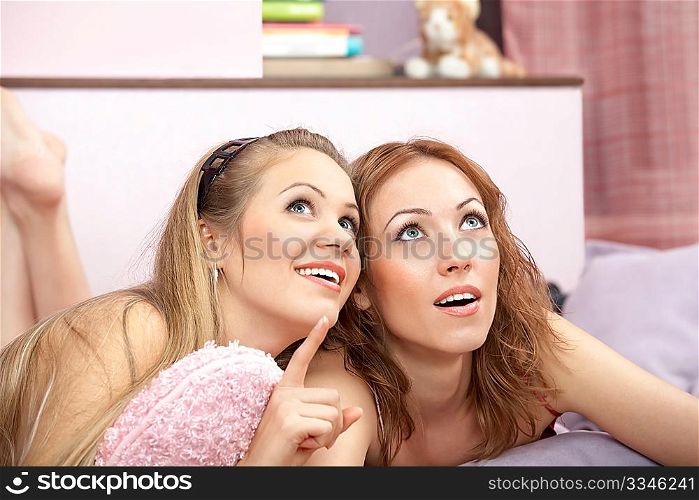 Two girlfriends lie on a sofa and consider something above