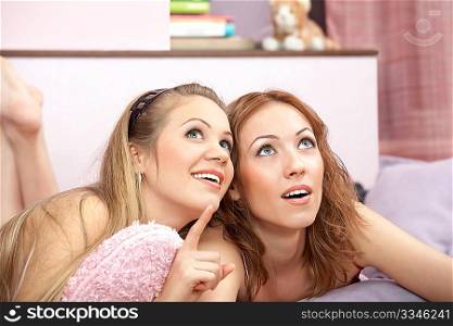 Two girlfriends lie on a sofa and consider something above