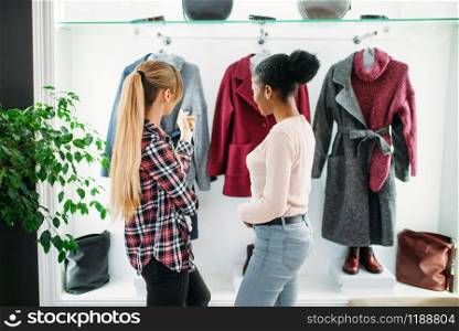 Two girlfriends looking at the coat in shop, shopping. Shopaholics in clothing store, consumerism lifestyle, fashion