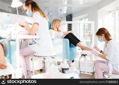 Two girlfriends on pedicure procedure in beauty salon. Professional beauticians and female customers, toenail care in spa studio