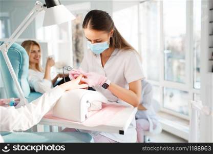 Two girlfriends relax on pedicure procedure in beauty salon. Professional beautician and female customers, nail care in spa studio, fingernail treatment. Girlfriends relax, pedicure in beauty salon