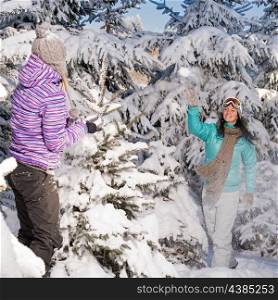 Two girlfriends throw snow balls winter forest enjoy holiday break
