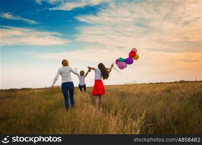 Two girls and one little boy running in field with balloons. Mother and her children. Family walking on the field