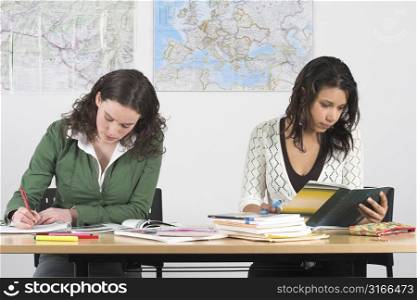 Two girls at school bend over their books