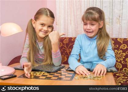 Two girls at the table collected montki one cries, the other laughs at it