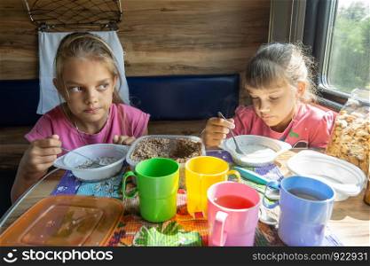 Two girls eat buckwheat with milk from plastic disposable tableware on a train
