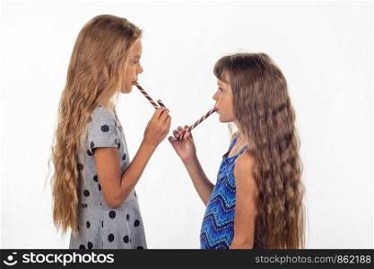 Two girls eating a cane shaped candy and turned to each other
