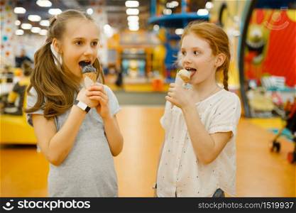 Two girls eats ice cream in the entertainment center. Children leisures on holidays, childhood happiness, happy kids on playground. Two girls eats ice cream in entertainment center