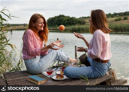 two girls enjoying picnic on a wooden pier on a shiny summer river shore