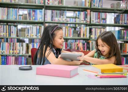 Two girls fighting for tablet in the classroom while reading books. People lifestyles and education. Young friendship and Kids relationship in school concept. Daycare and diversity theme