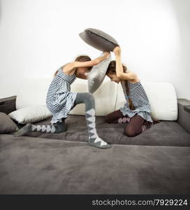 Two girls fighting with cushions on couch