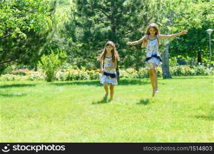 Two girls have fun running on the green lawn in the park
