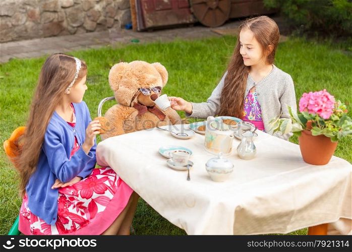 Two girls having tea party with teddy bear at yard