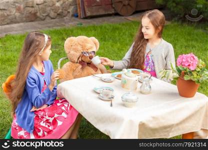 Two girls having tea party with teddy bear at yard