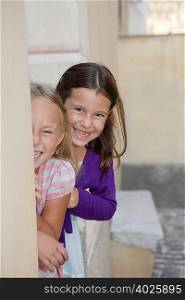 two girls hiding behind wall, laughing