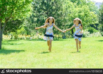 Two girls holding hands run on a green lawn in a park