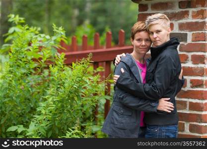 Two girls hugging front of fence and they look toward camera, horizon format