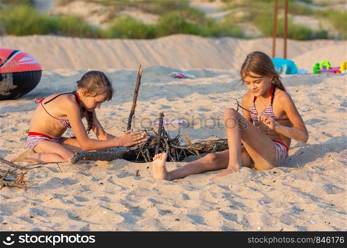 Two girls in the evening on the beach prepare a place for a fire