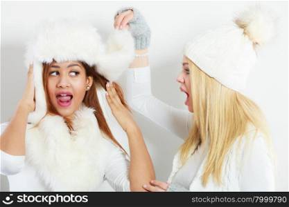 Two girls in winter clothing whispering secret. Wintertime relationship and gossip concept. Two girls blonde and mixed race in winter clothing warm cap whispering secret surprised face expression.