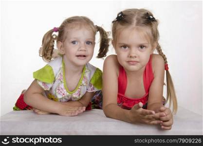 Two girls lie on your stomach, leaning on his hands and looking in the frame. Studio light background