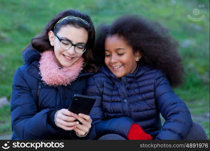 Two girls looking at the mobile in the park.