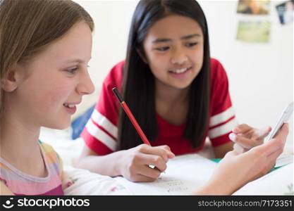 Two Girls Lying On Bed Using Mobile Phone To Help With Homework