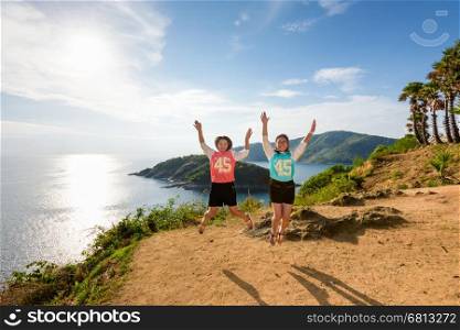 Two girls mother and daughter jumping with happy on the mountain at panoramic ocean and island viewpoint of Cape Phromthep in Phuket, Thailand