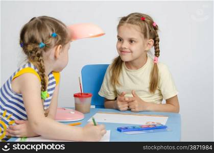 Two girls of four and six years of sitting at the table and draws and paints and pencils. Two girls drawing a table looking at each other