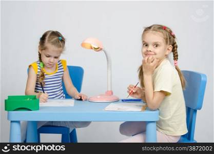 Two girls of four and six years of sitting at the table and draws and paints and pencils. Two sisters draw sitting at the table