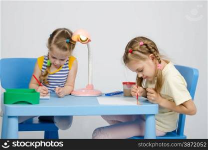 Two girls of four and six years of sitting at the table and draws and paints and pencils. Two girls drawing at table draw paints and pencils