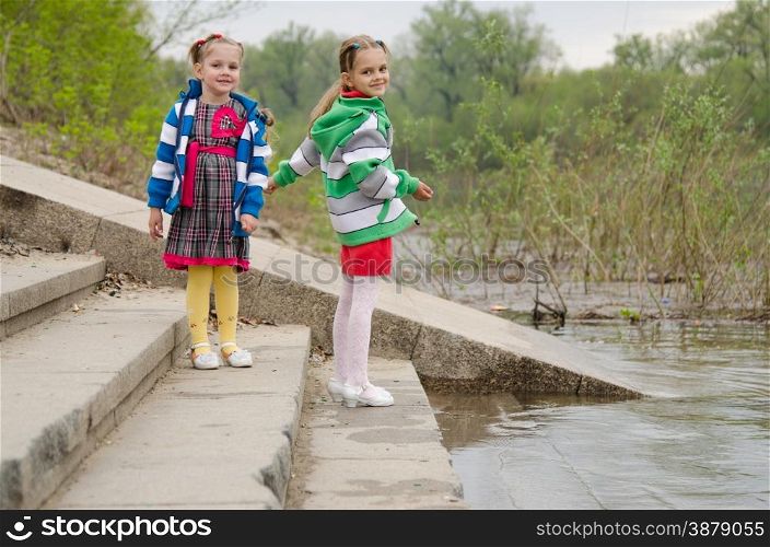 two girls of four and six years of walking on the embankment of the river. Two girls standing on the steps near water