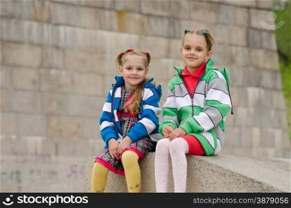 two girls of four and six years of walking on the embankment of the river. Sisters sitting on a granite ramp