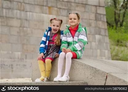 two girls of four and six years of walking on the embankment of the river. Two girls sit on a granite staircase