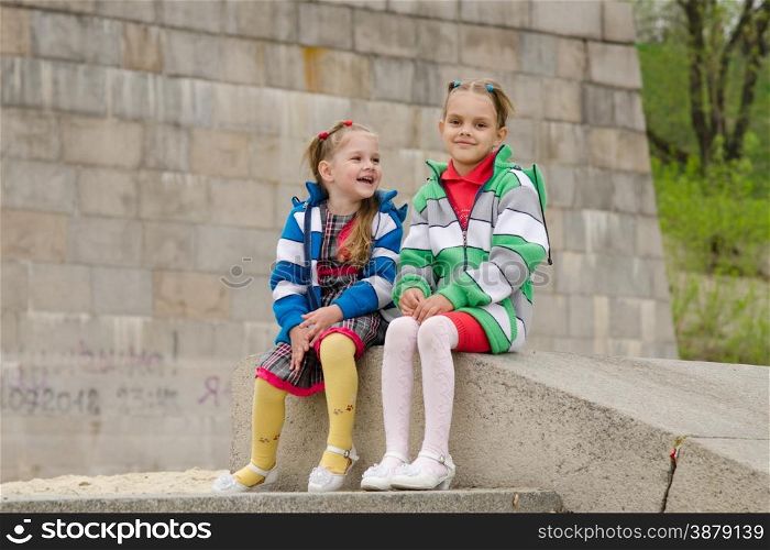 two girls of four and six years of walking on the embankment of the river. Two girls sit on a granite ramp