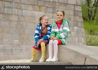 two girls of four and six years of walking on the embankment of the river. Two girls sit on a granite ramp