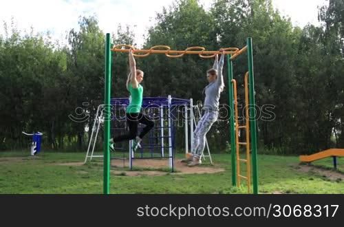 Two girls on sports ground making leg-split in the air hanging on sport equipment.
