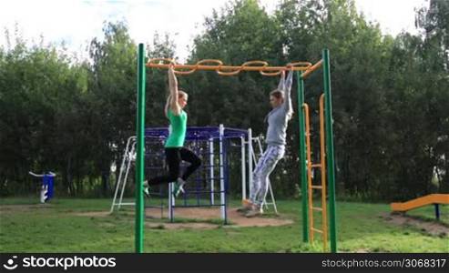 Two girls on sports ground making leg-split in the air hanging on sport equipment.