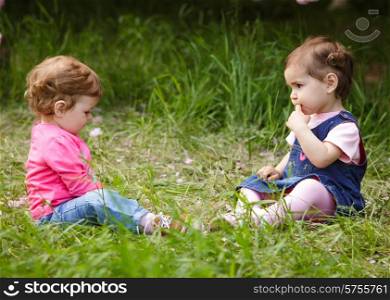 Two girls play in the garden, sitting on the grass