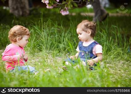 Two girls play in the garden, sitting on the grass