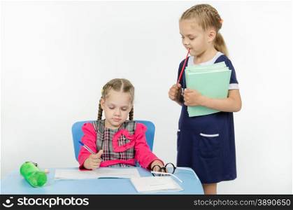 Two girls play school teacher and student. Girl teacher enthusiastically looking at the notebook student