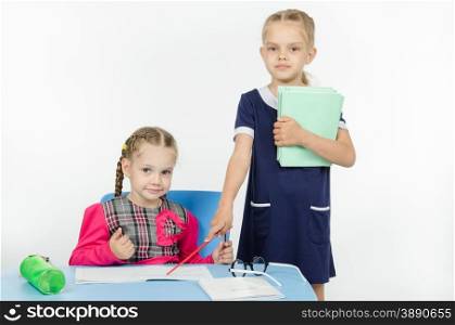 Two girls play school teacher and student. Girl teacher points at student notebook