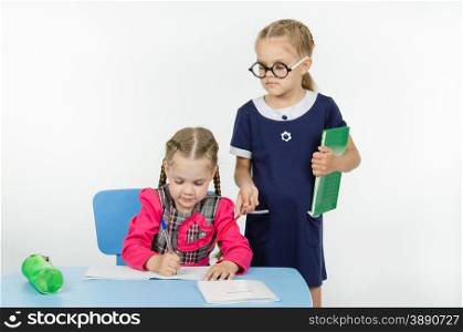 Two girls play school teacher and student. Girl teacher supervises the job apprentice