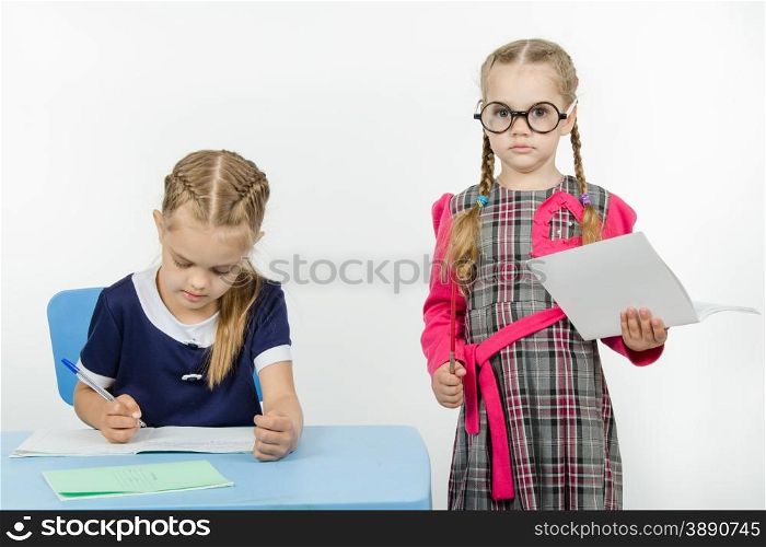 Two girls play school teacher and student. Severe teacher standing at the student