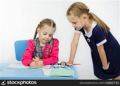 Two girls play school teacher and student. Teacher student leaning on a table looking notebook